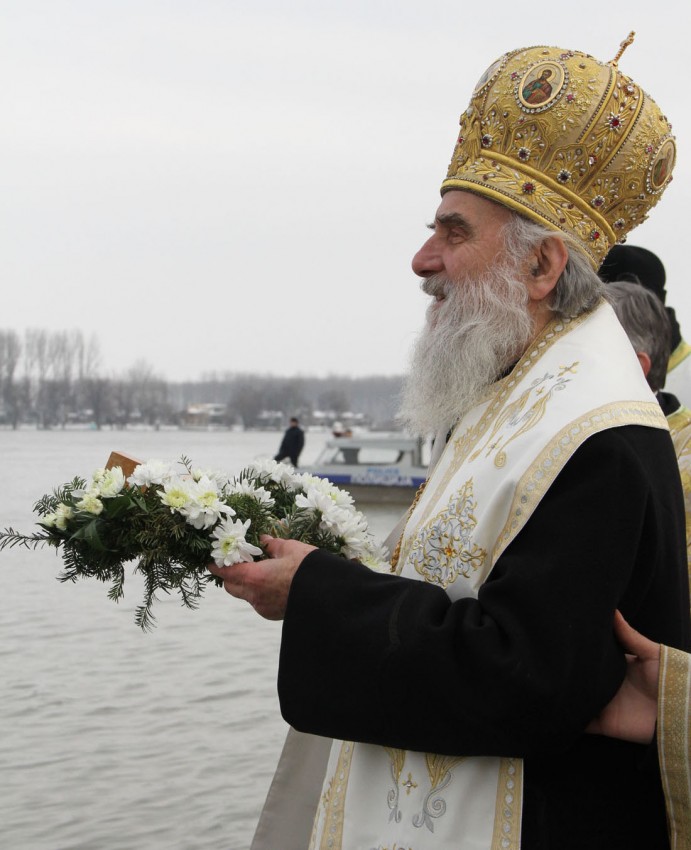Patriarch Irinej of Serbia is throwing the cross in the water. 