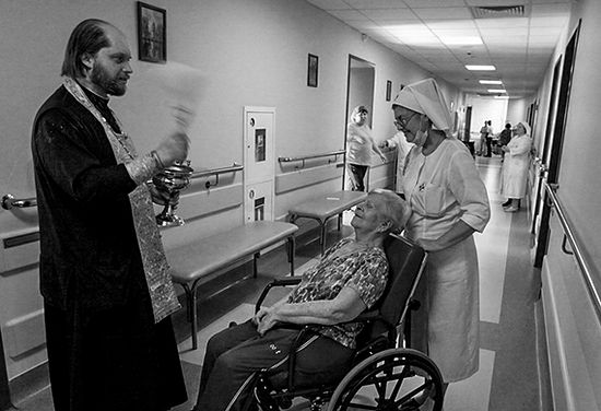Священник Иоанн Емельянов кропит больную в 1-й градской больнице