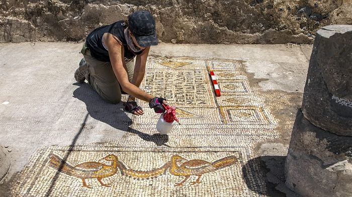 Jessica Rentz cleans a pair of birds holding a garland, foreground, and one of the dedication inscriptions in the mosaic, rear, of the Burnt Church in July 2019. Photo by Dr. Michael Eisenberg