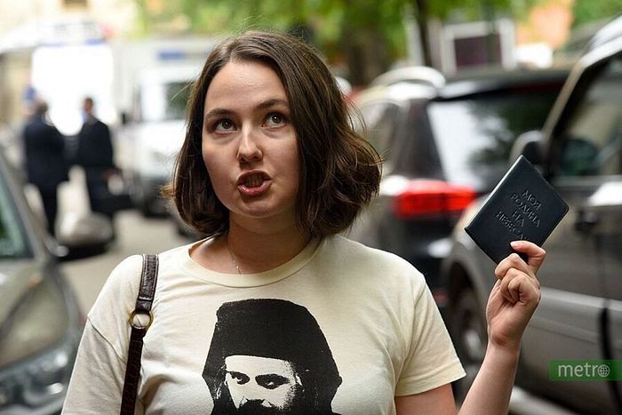 Ludmila holding her passport outside a court case for destroying a blasphemous art display. The cover of her passport reads "My home is in Heaven," reflecting Fr. Daniel's teaching on uranopolitism.