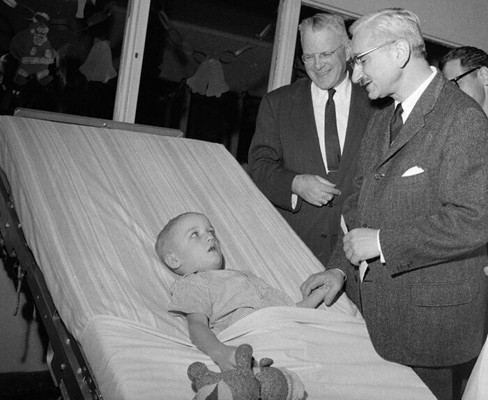 Σε αυτή την φωτογραφία του 1959, ο ιατρός Άλμπερτ Σέιμπιν (δεξιά), του οποίου το εμβόλιο κατά της πολιομυελίτιδας δοκιμάζονταν ευρέως σε όλο τον κόσμο, βρίσκεται στο παιδικό νοσοκομείο της πολιτείας Σινσινάτι με τον 5χρονο Μαρκ Στέισι, ο οποίος είχε προσβληθεί από την παραλυτική πολιομυελίτιδα, λίγους μήνες νωρίτερα. Μαζί του είναι ο ιατρός Βάλτερ Λάνγκσαμ, Πρόεδρος του Πανεπιστημίου Σινσινάτι. Φωτογραφία: Harvey Eugene Smith/АР/www.statnews.com