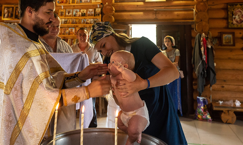 Η βάπτιση νηπίου, Αύγουστος 2021, χωριό Ζαβέτνογιε. Η μαμά κρατάει το παιδί πάνω από την κολυμβήθρα. Παρόντες στην εκκλησία οι νονοί. Ο πατέρας του παιδιού χαμογελάει από ευτυχία.
