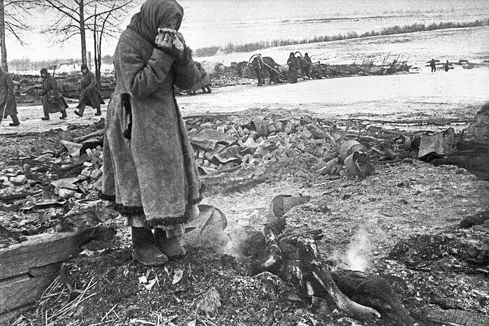 Пожилая женщина у сгоревших останков родных, убитых фашистами при отступлении из деревни Большево Смоленской области
