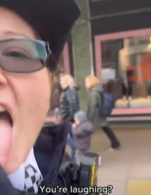 Волонтер лондонской полиции показала язык на камеру после того, как Х. Лондон начала отстаивать свое право петь на улице. Фото: YouTube/HarmonieLondon